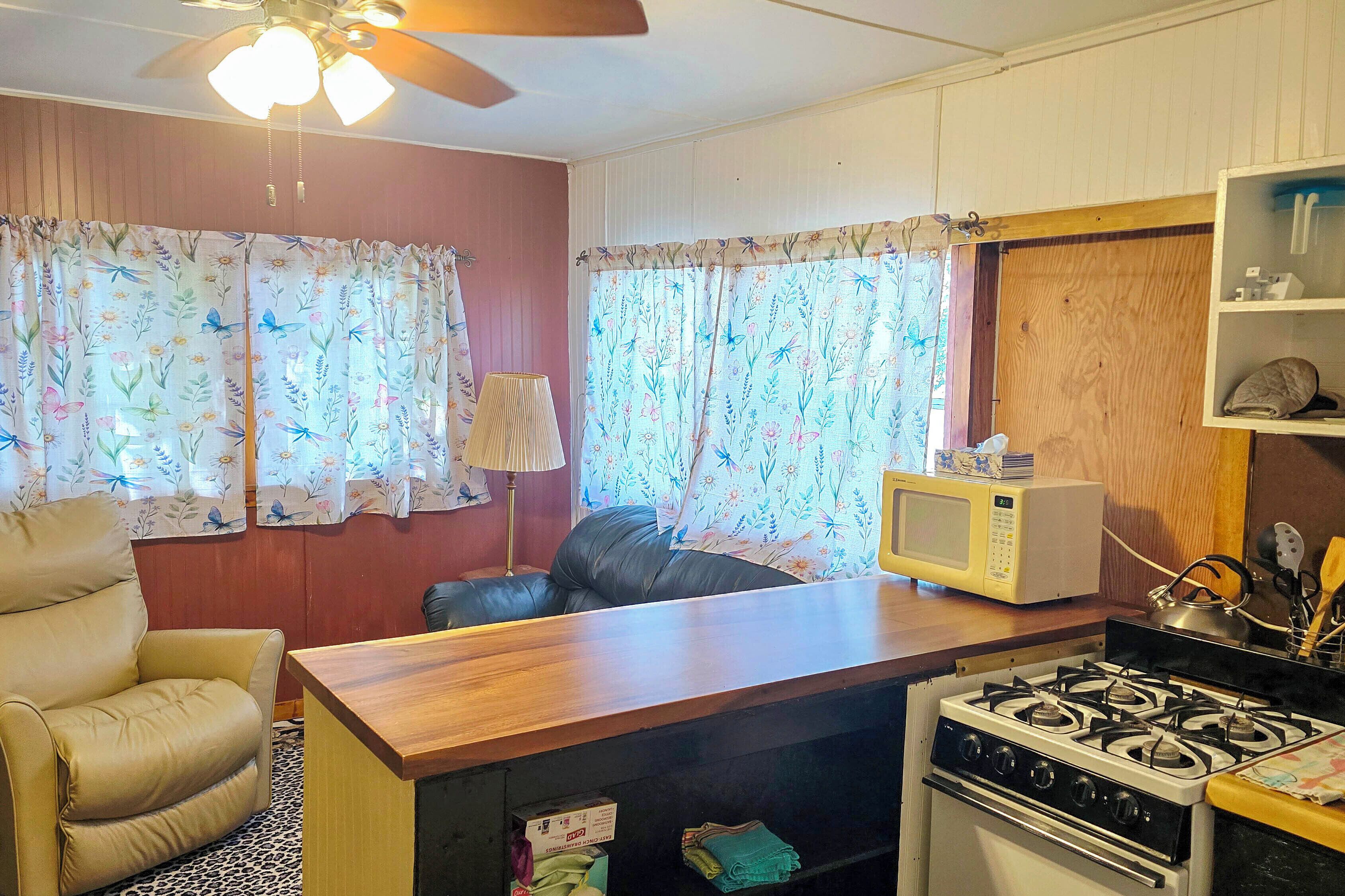 Cocina compacta con estufa, microondas y un pequeño comedor con una silla y una mesa.