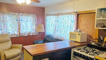 Cocina compacta con estufa, microondas y un pequeño comedor con una silla y una mesa.