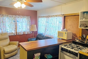 A compact kitchen with a stove, microwave, and a small dining area with a chair and table.