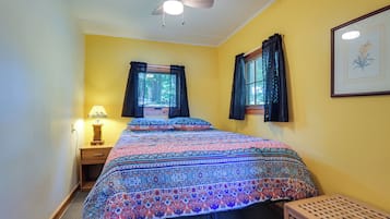Un dormitorio con una cama, una ventana con cortinas, un ventilador de techo y una lámpara.