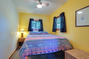 A bedroom with a bed, a window with curtains, a ceiling fan, and a lamp.