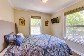 A bedroom with a large bed, two windows with blinds, a flat-screen TV mounted on the wall, and a ceiling light fixture. - Walk to Historic Dtwn Tuskegee! Apt w/ Shared Yard (Tuskegee)
