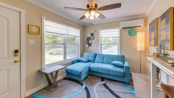 A room with a sectional sofa, a ceiling fan, a clock, and a window with blinds.