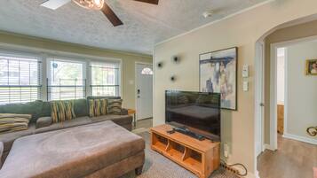 A living room with a sofa, ottoman, TV, and artwork on the wall.