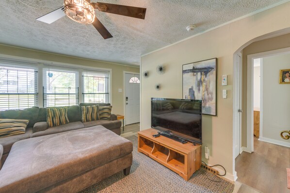 A living room with a sofa, ottoman, TV, and artwork on the wall.