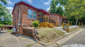 A two-story brick house with a red roof, a front porch, and a wooden staircase leading to the entrance.