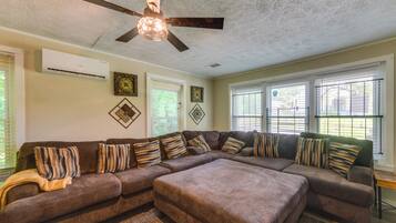 A living room with a sectional sofa, patterned cushions, a ceiling fan, and decorative wall art.