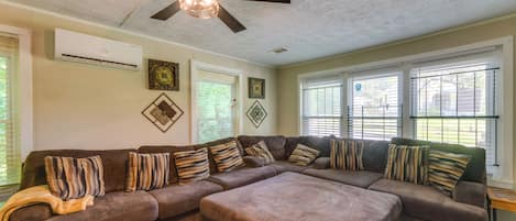 A living room with a sectional sofa, patterned cushions, a ceiling fan, and decorative wall art.