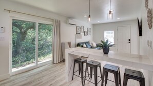 A modern kitchen with a marble countertop, bar stools, pendant lighting, and a large sliding glass door leading to a garden. - Mtn-view Deck w/ Grill! Modern Medicine Park Cabin (Medicine Park)