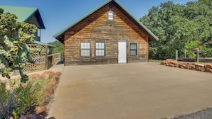 A log cabin with a front porch, a garage, and a clear sky. - Mtn-view Deck w/ Grill! Modern Medicine Park Cabin (Medicine Park)