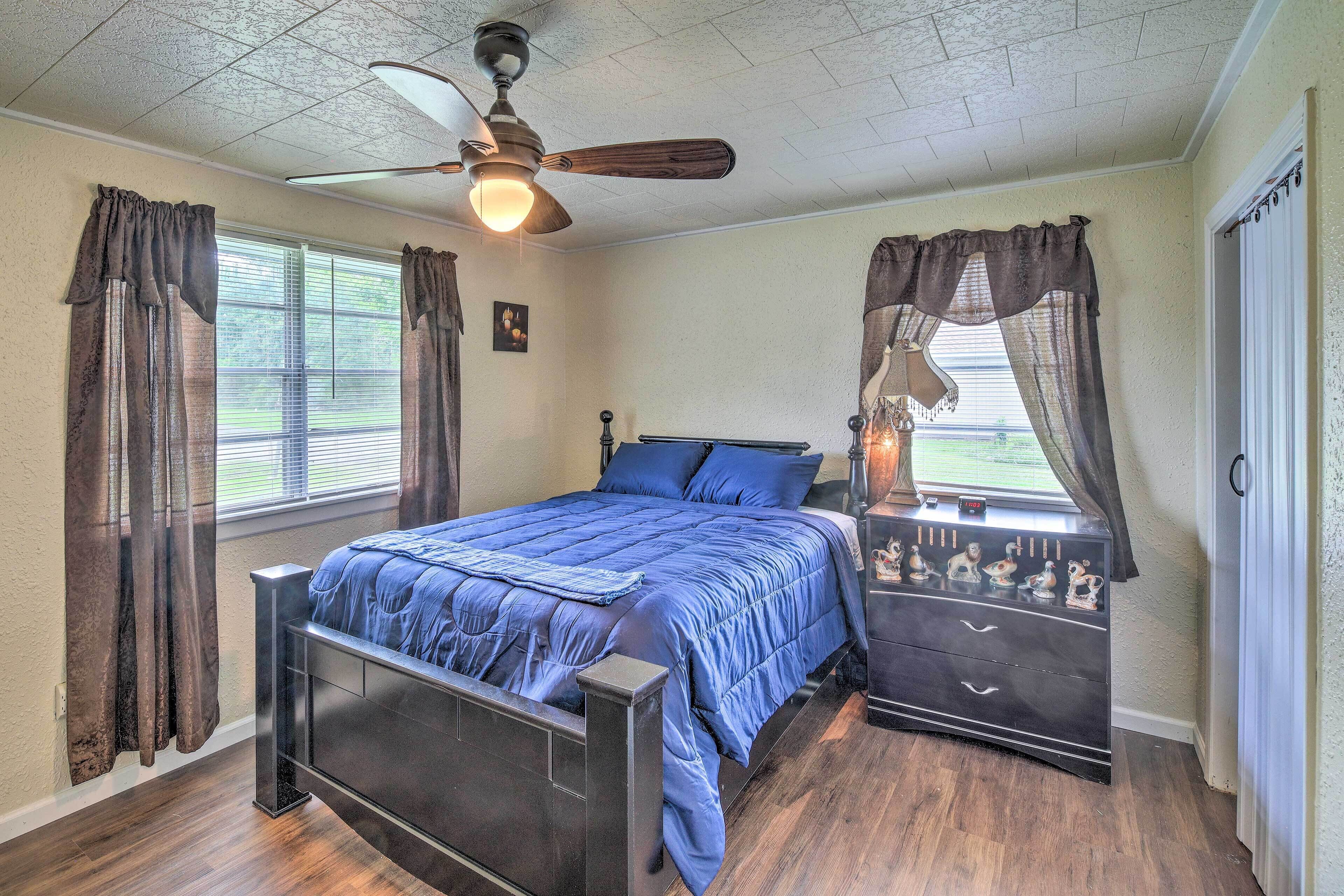 Une chambre à coucher avec un lit, une table de chevet, un ventilateur de plafond et une fenêtre avec des rideaux.