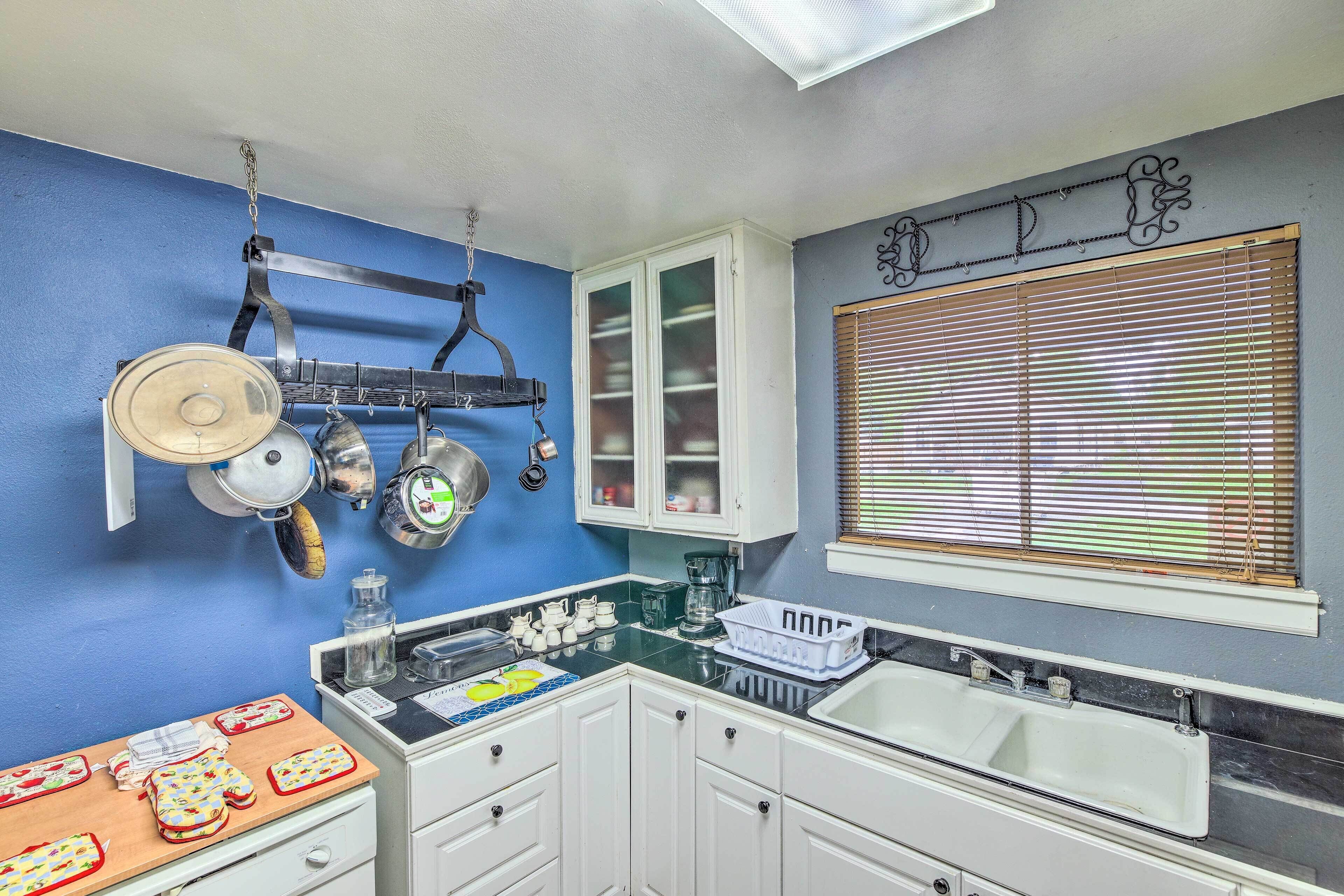 A kitchen with white cabinets, a black countertop, and a window with blinds.