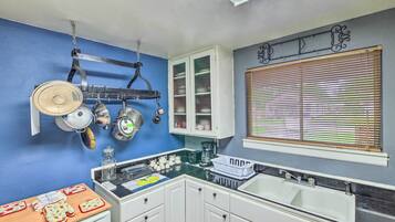 A kitchen with white cabinets, a black countertop, and a window with blinds.