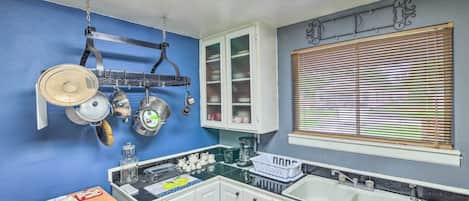 A kitchen with white cabinets, a black countertop, and a window with blinds.