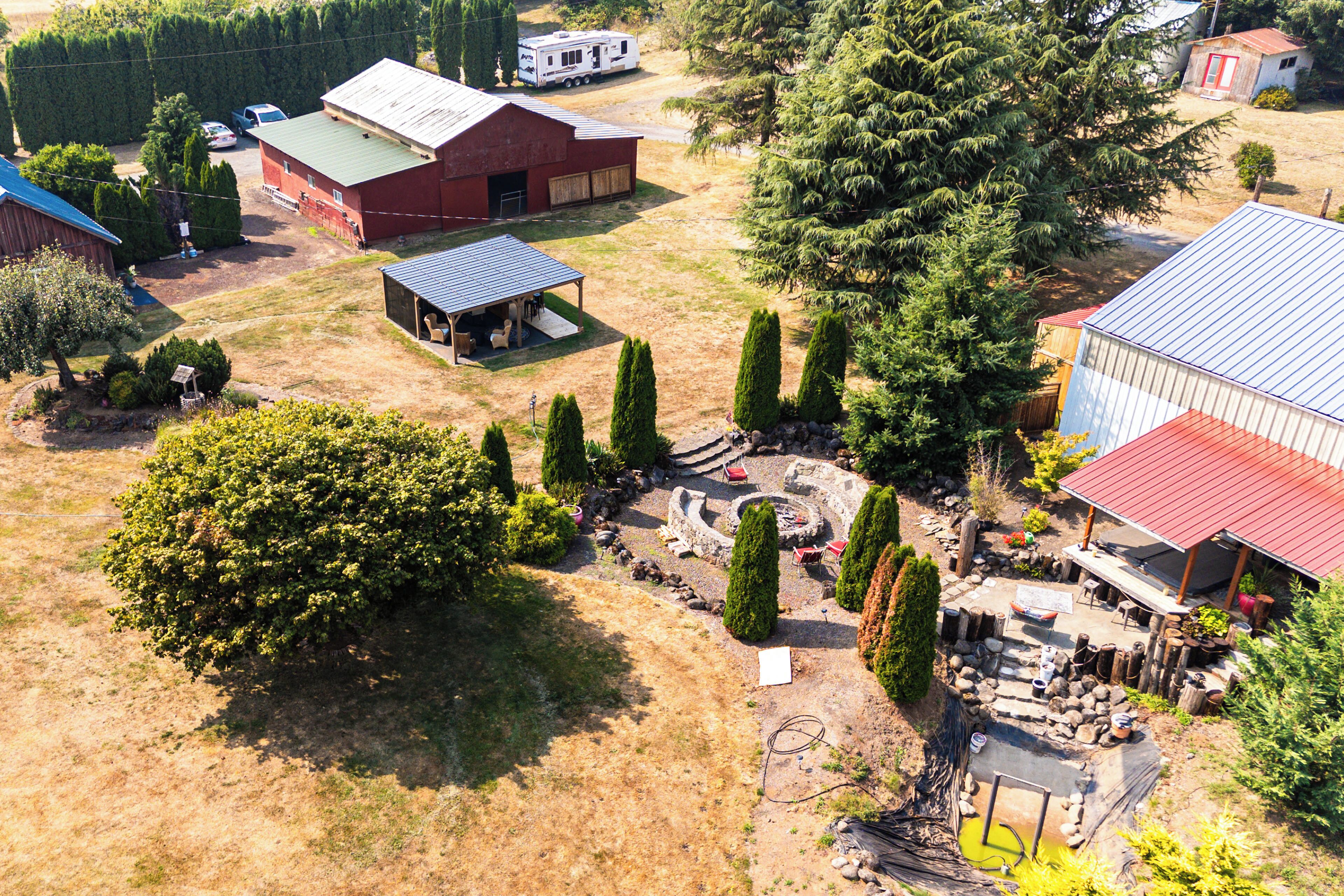 An aerial view of a property with a large open yard, a covered outdoor seating area, and multiple buildings with red roofs.