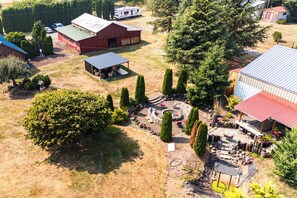 An aerial view of a property with a large open yard, a covered outdoor seating area, and multiple buildings with red roofs.