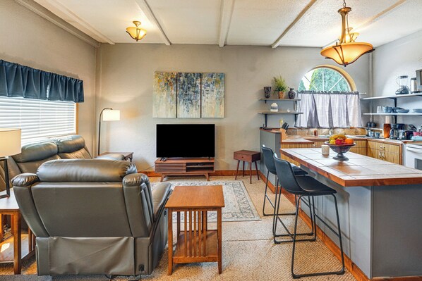 A modern living room with a flat-screen TV, leather sofa, and a dining area with bar stools.