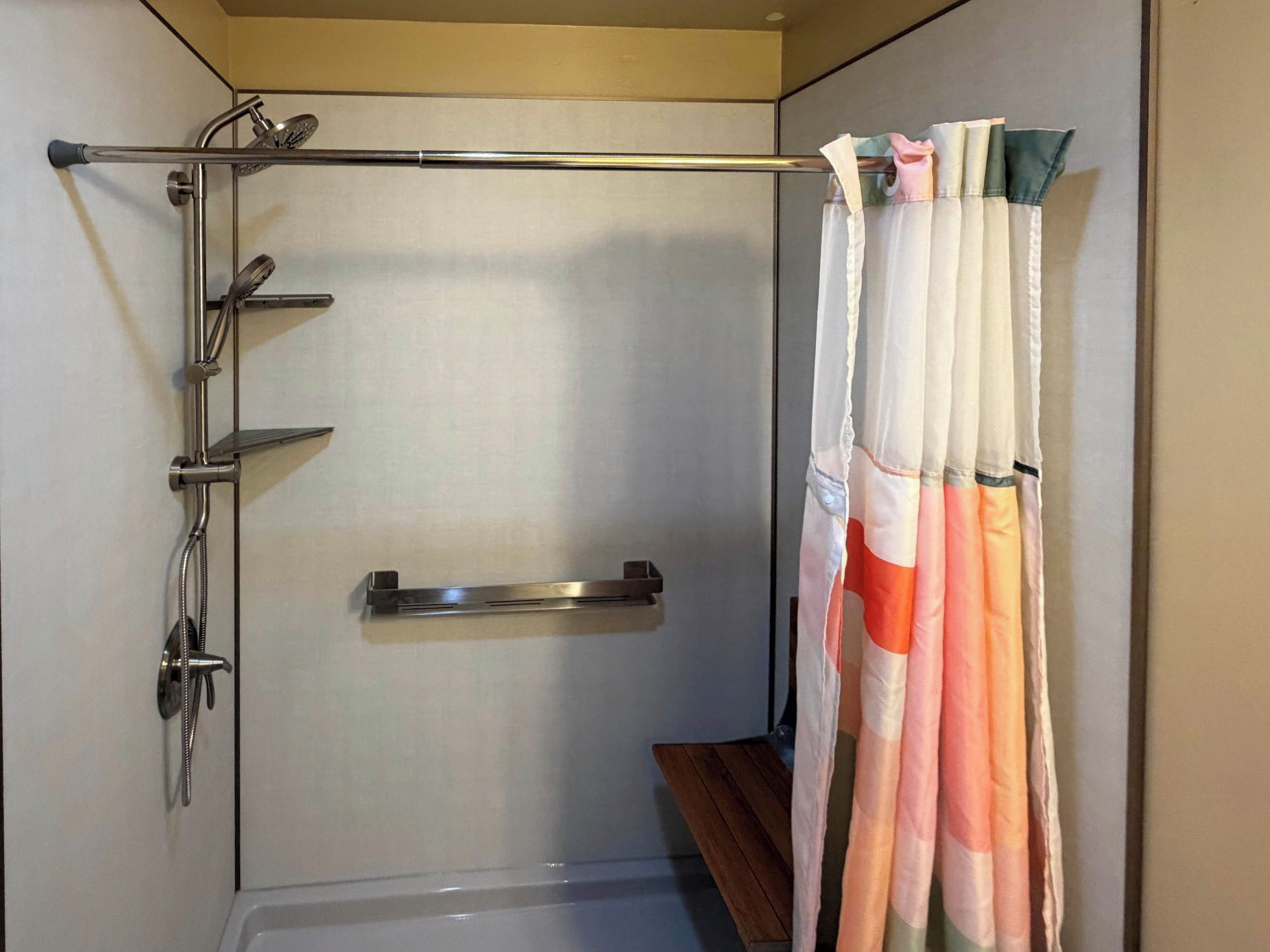 A shower area with a glass door, a metal grab bar, and a wooden bench.
