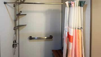 A shower area with a glass door, a metal grab bar, and a wooden bench.