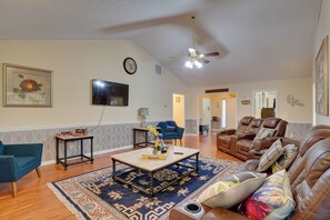 A living room with a ceiling fan, a flat-screen TV, a coffee table with decorative items, a sofa, and a reclining chair. - Hot Tub & Deck! Loganville Group Retreat (Loganville)
