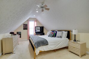 A bedroom with a sloped ceiling, a bed with a grey blanket, a bedside table with a lamp, a dresser, and a vanity with a mirror. - Hot Tub & Deck! Loganville Group Retreat (Loganville)