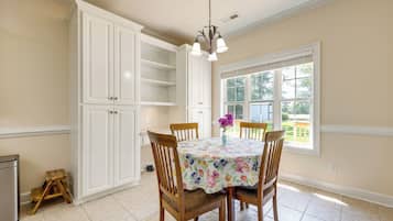 A dining area with a table set for four, surrounded by wooden chairs, a floral tablecloth, and a vase with flowers.