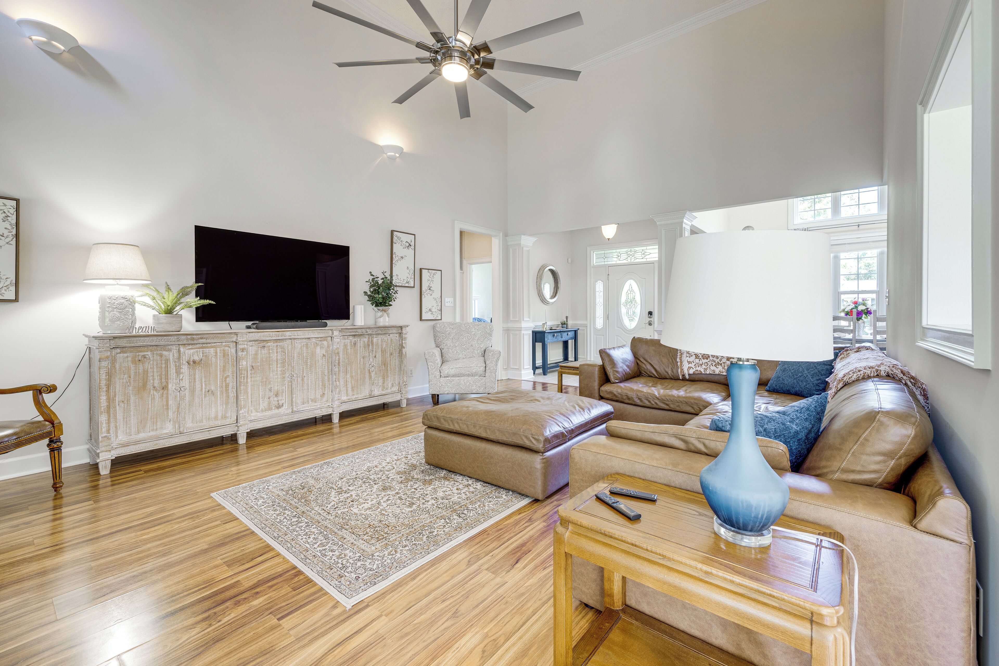 A spacious living room with a flat-screen TV, a ceiling fan, a sofa set, a coffee table, and a decorative vase.