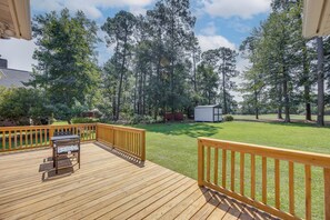 A wooden deck with a table and chairs, surrounded by a grassy yard and trees.