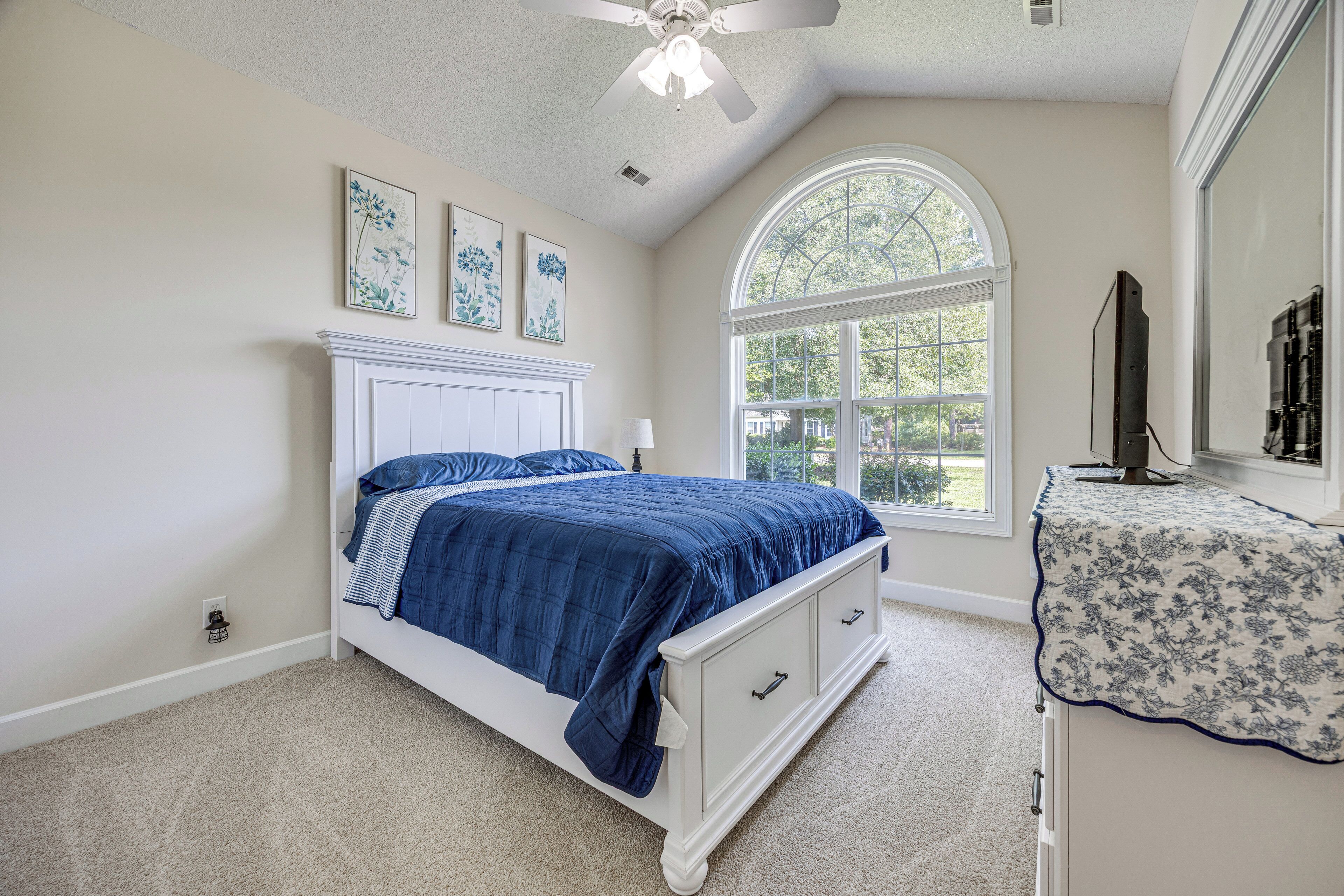 A bedroom with a bed, a dresser, a window, and ceiling fans.