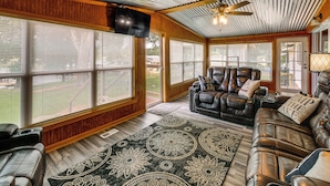 A spacious living room with a large window, a ceiling fan, and a leather sofa with decorative pillows. - Dock & Outdoor Bar! Lake Blackshear Getaway (Cobb)
