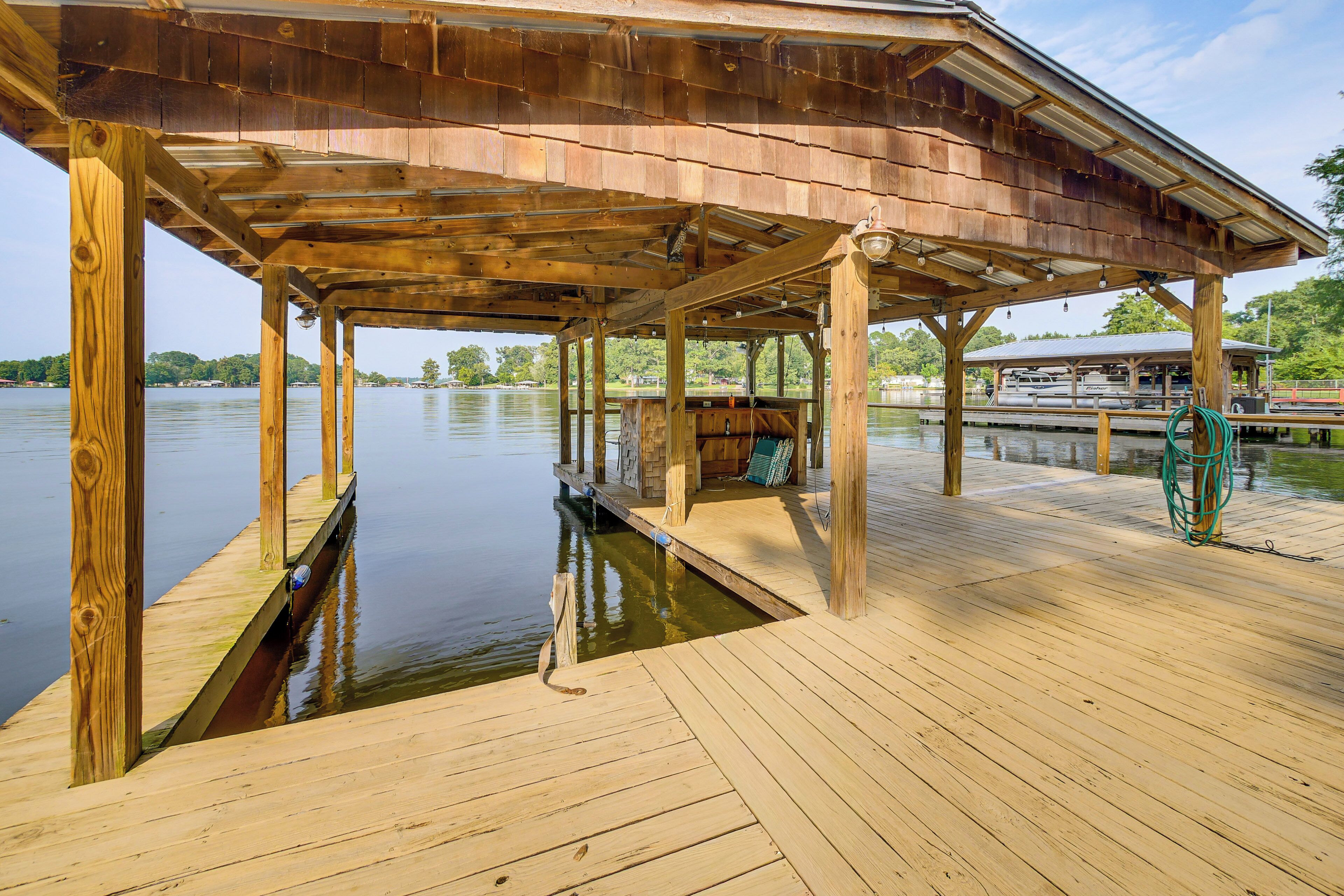 A wooden dock extending into a calm lake, with a covered seating area and a boat docked on the right.