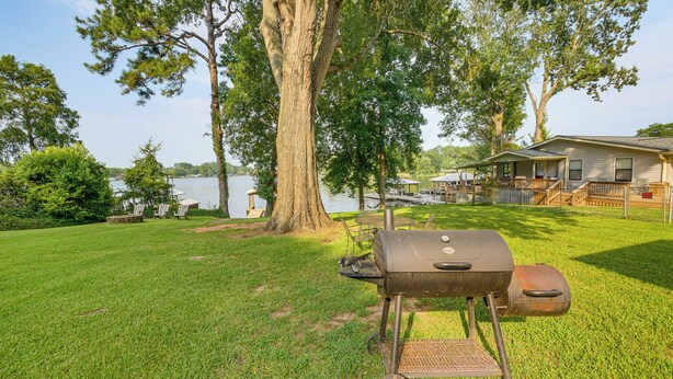 A backyard with a grill, a wooden deck, and a house by a lake. - Dock & Outdoor Bar! Lake Blackshear Getaway (Cobb)