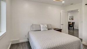 Un dormitorio con cama, mesita de noche, ventilador de techo y puerta que da a un comedor.