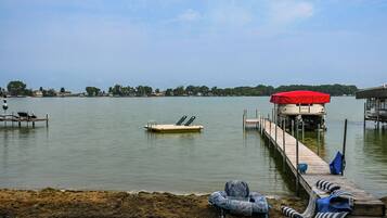 A lakeside dock with a red canopy, lounge chairs, and a small boat.