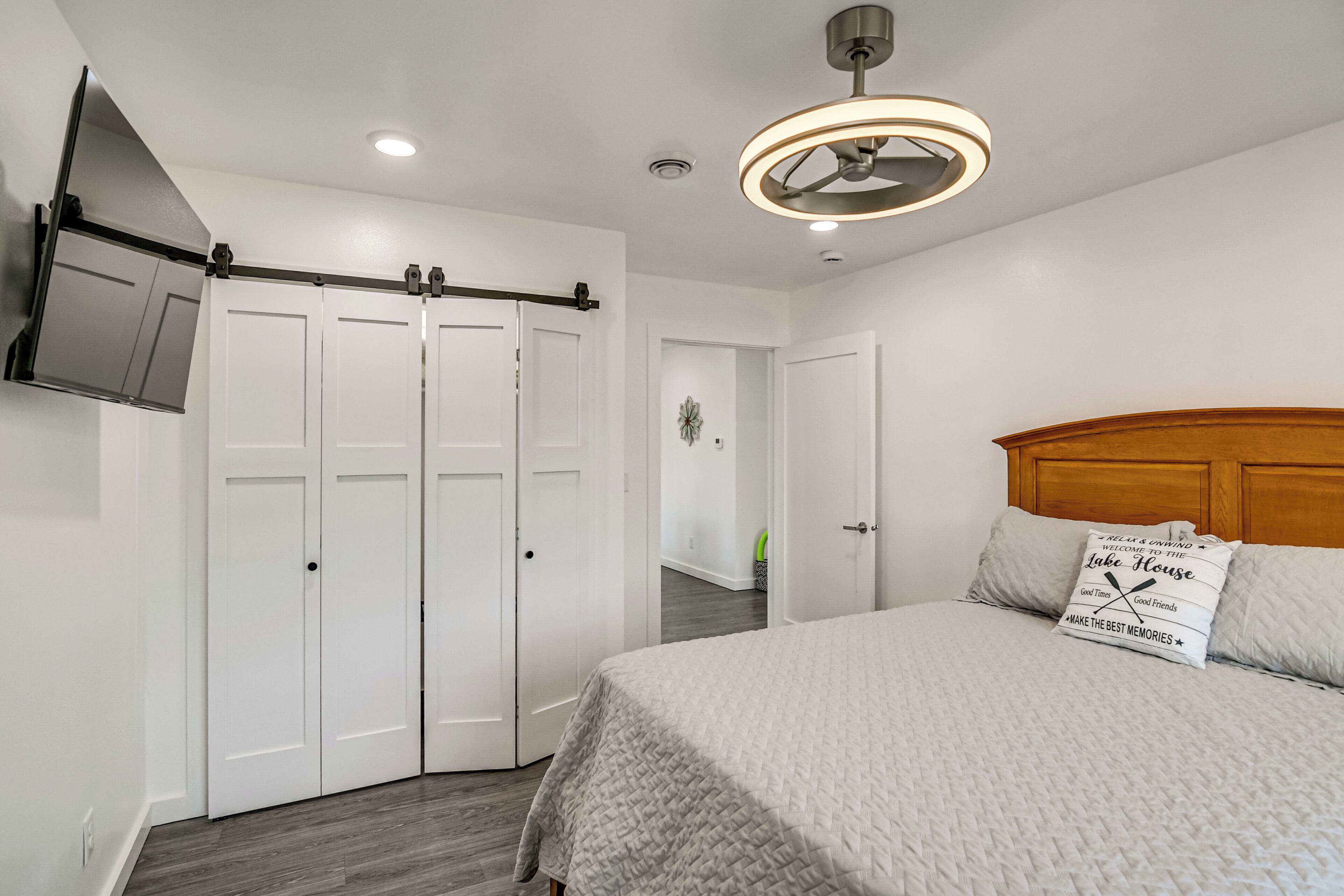 A bedroom with a bed, a ceiling fan, a wall-mounted TV, and a sliding door closet.