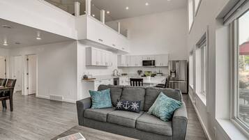 A modern living room with a grey sofa, a coffee table with books, and a view of the kitchen in the background.