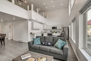 A modern living room with a grey sofa, a coffee table with books, and a view of the kitchen in the background.