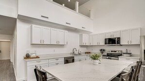 Una cocina moderna con armarios blancos, una isla grande, electrodomésticos de acero inoxidable y un comedor con sillas.