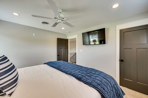 Un dormitorio con cama, ventilador de techo, iluminación empotrada, televisor y una puerta.