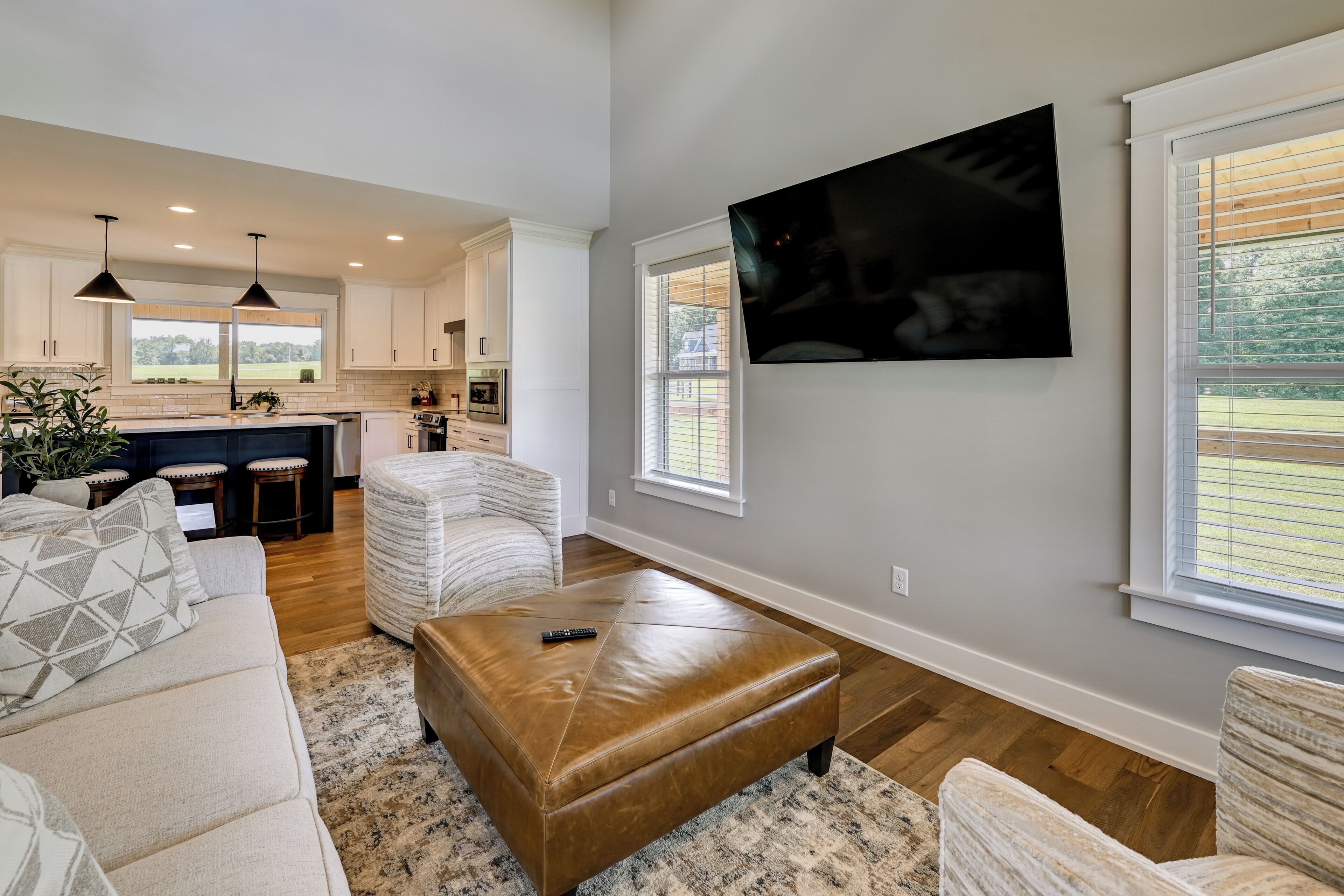 A modern living room with a brown leather ottoman, a white sofa, and a large flat-screen TV mounted on the wall.
