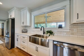 Una cocina moderna con armarios blancos, electrodomésticos de acero inoxidable, un amplio ventanal y un lavavajillas integrado.