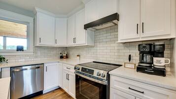 A modern kitchen with white cabinetry, a stainless steel dishwasher, a built-in oven, and a coffee maker.