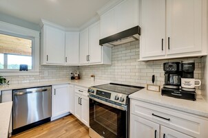 A modern kitchen with white cabinetry, a stainless steel dishwasher, a built-in oven, and a coffee maker.