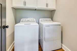A laundry room with two white appliances, one dryer and one washer, under white cabinets.