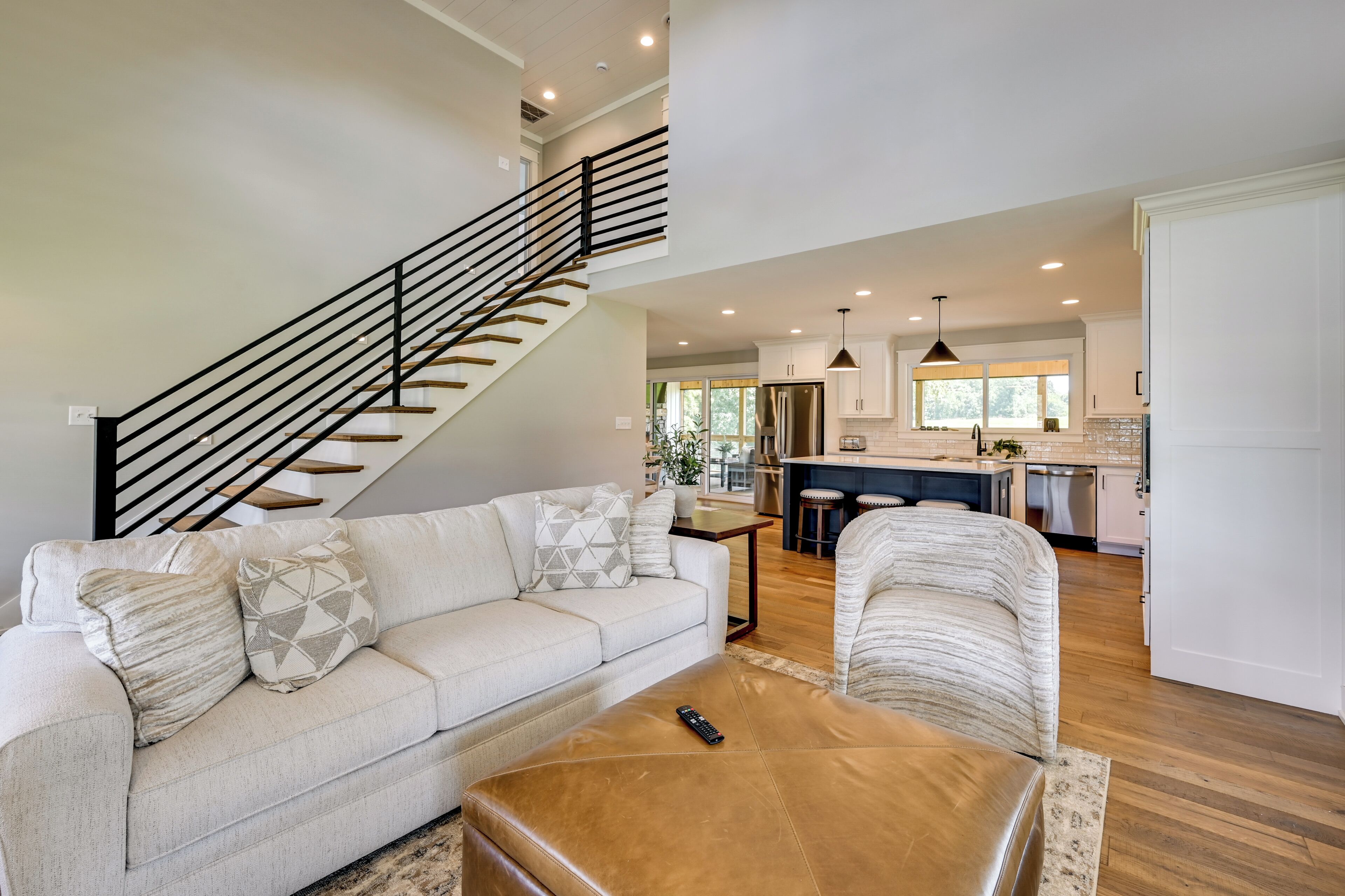 A spacious living room with a staircase, a sofa, a coffee table, and a kitchen area in the background.