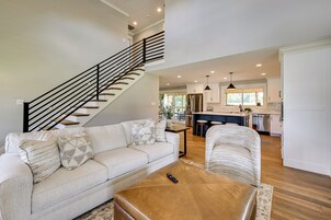 A spacious living room with a staircase, a sofa, a coffee table, and a kitchen area in the background.