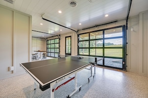 A ping pong table in a room with a large window and a door leading outside.