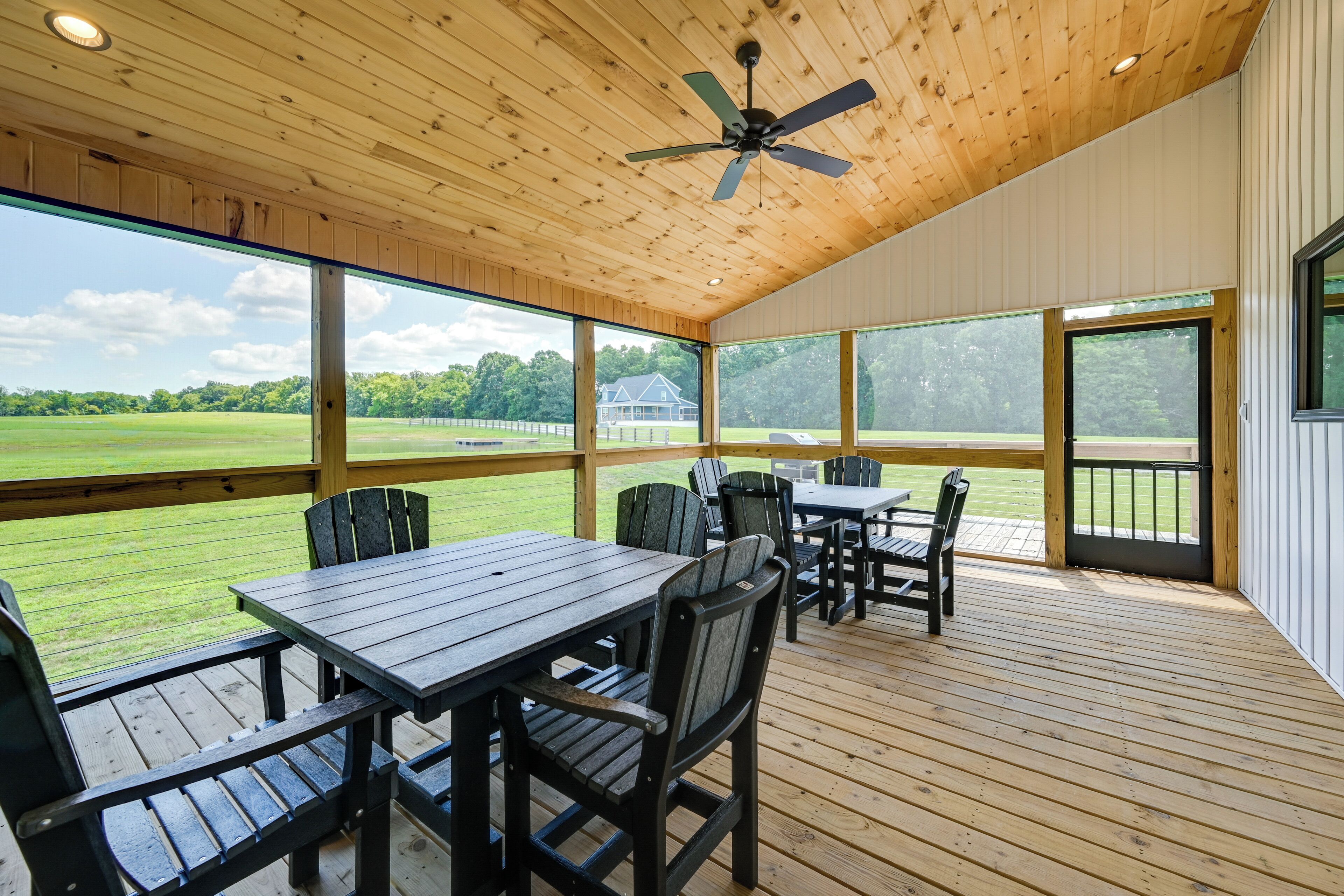 A covered outdoor area with wooden flooring, tables, chairs, and a ceiling fan.