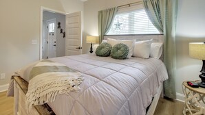 A bedroom with a bed, a bedside table, a lamp, and a window with curtains.