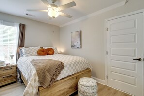 A bedroom with a bed, a nightstand, a lamp, a ceiling fan, a door, and a window with curtains. - Large Patio w/ Fire Pit, Grill! Springfield Home (Springfield)